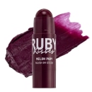 A imagem mostra um blush em bastão (stick), e ao fundo uma amostra do produto em fundo branco indicando cor e textura.