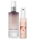 Produtos de cuidados capilares da marca Braé. Um frasco spray rosa claro com o rótulo "Essential Hair Repair Spray" para reparação capilar. Um frasco maior de vidro fosco na cor roxa com o rótulo "Beauty Sleep" descrito como um sérum noturno nutritivo.