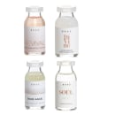 A imagem mostra quatro frascos de vidro transparente da marca Brae, contendo diferentes produtos de tratamento capilar. Os frascos têm tampas brancas e rótulos com o nome da marca e do produto.