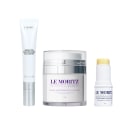 Três produtos da marca Le Moritz: um tubo de creme redutor de linhas, um pote de creme antirrugas multicamadas e um bastão rejuvenescedor. Embalagens brancas com detalhes em roxo e amarelo, exibindo os nomes e descrições dos produtos.