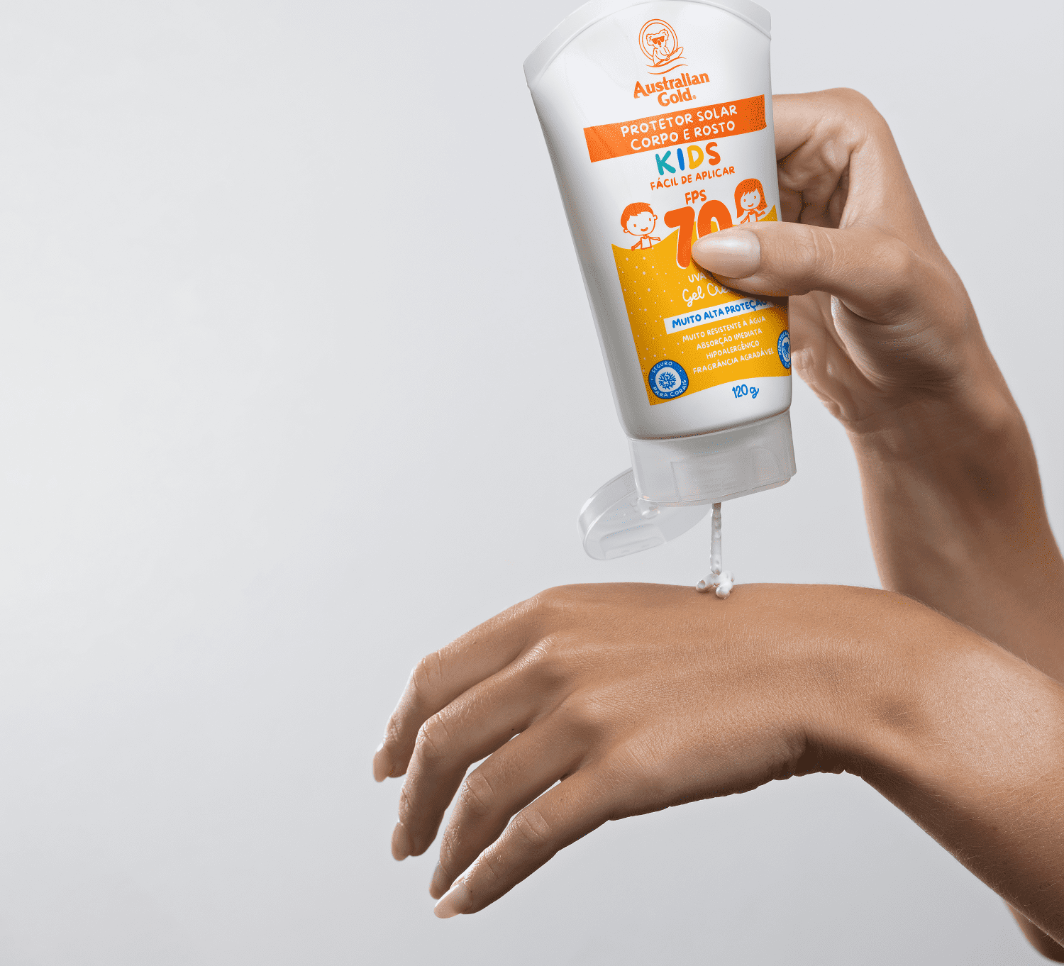 Tubo com aproximadamente 100g de produto sendo segurado por uma mão feminina. Cores vibrantes e design voltado para o público infantil.