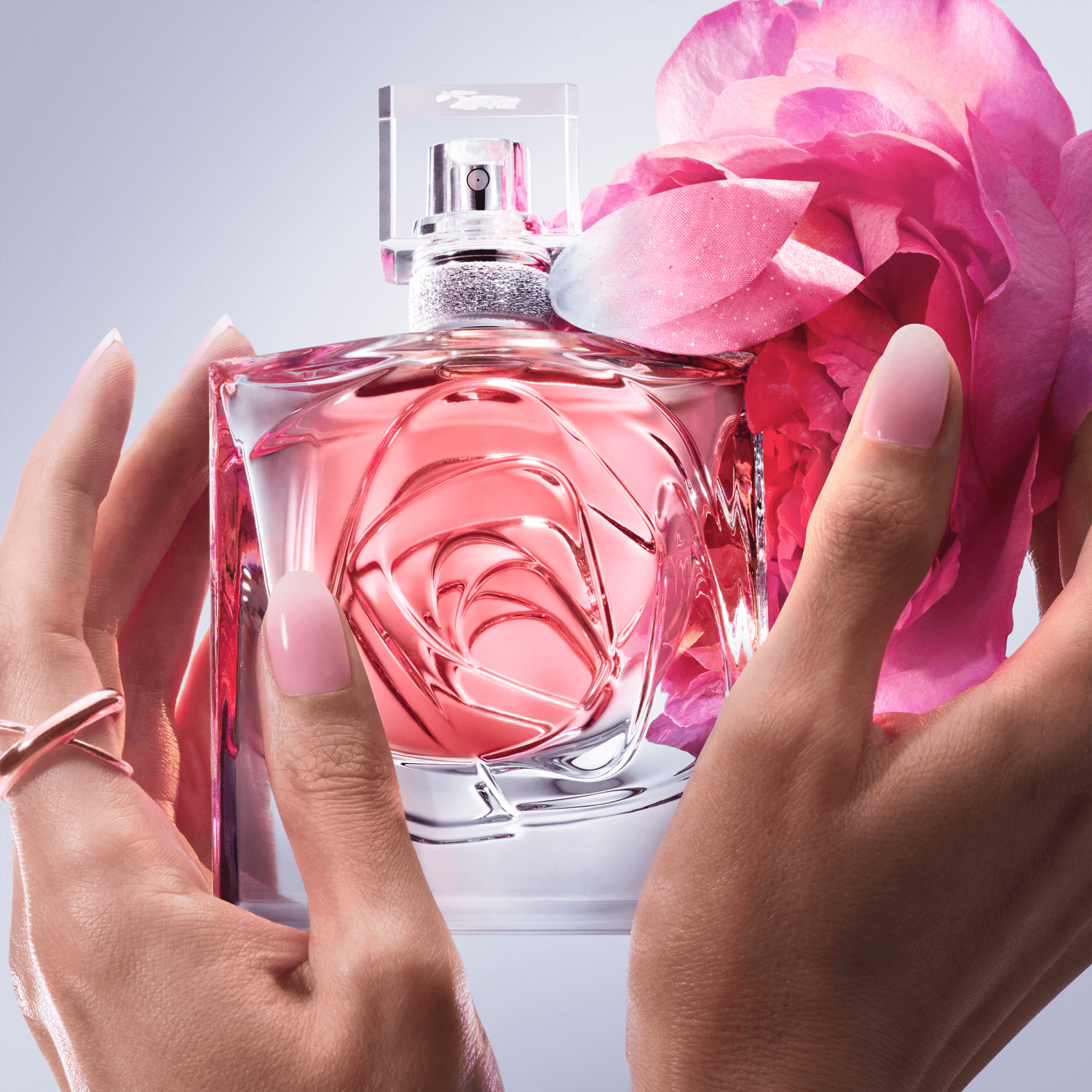 Frasco de perfume Lancôme com design floral em vidro transparente, tampa prateada e detalhe em rosa. Embalagem elegante e sofisticada em tons de rosa e branco.