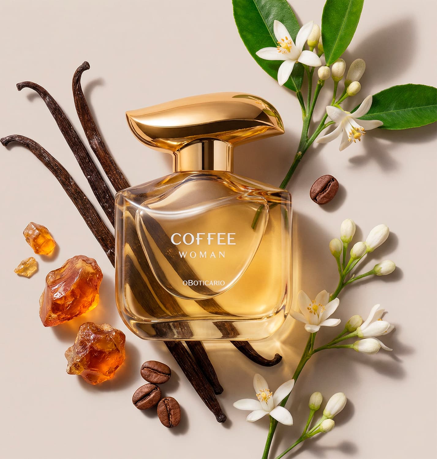 Imagem de um frasco dourado com tampa da mesma tonalidade do desodorante colônia Coffee Woman Floriental Ambarado sobre superfície bege, com flores brancas, grãos de café e pedras âmbar ao redor, em ambiente com tons neutros.