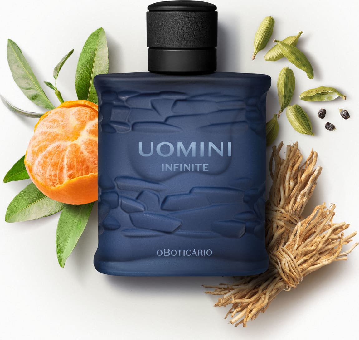 Frasco retangular azul marinho com texturas onduladas, tampa preta e letras com degradê em tons de azul de desodorante colônia da marca Uomini Infinite rodeado por gomos de bergamota, folhas verdes, vagens de cardamomo e raízes secas.