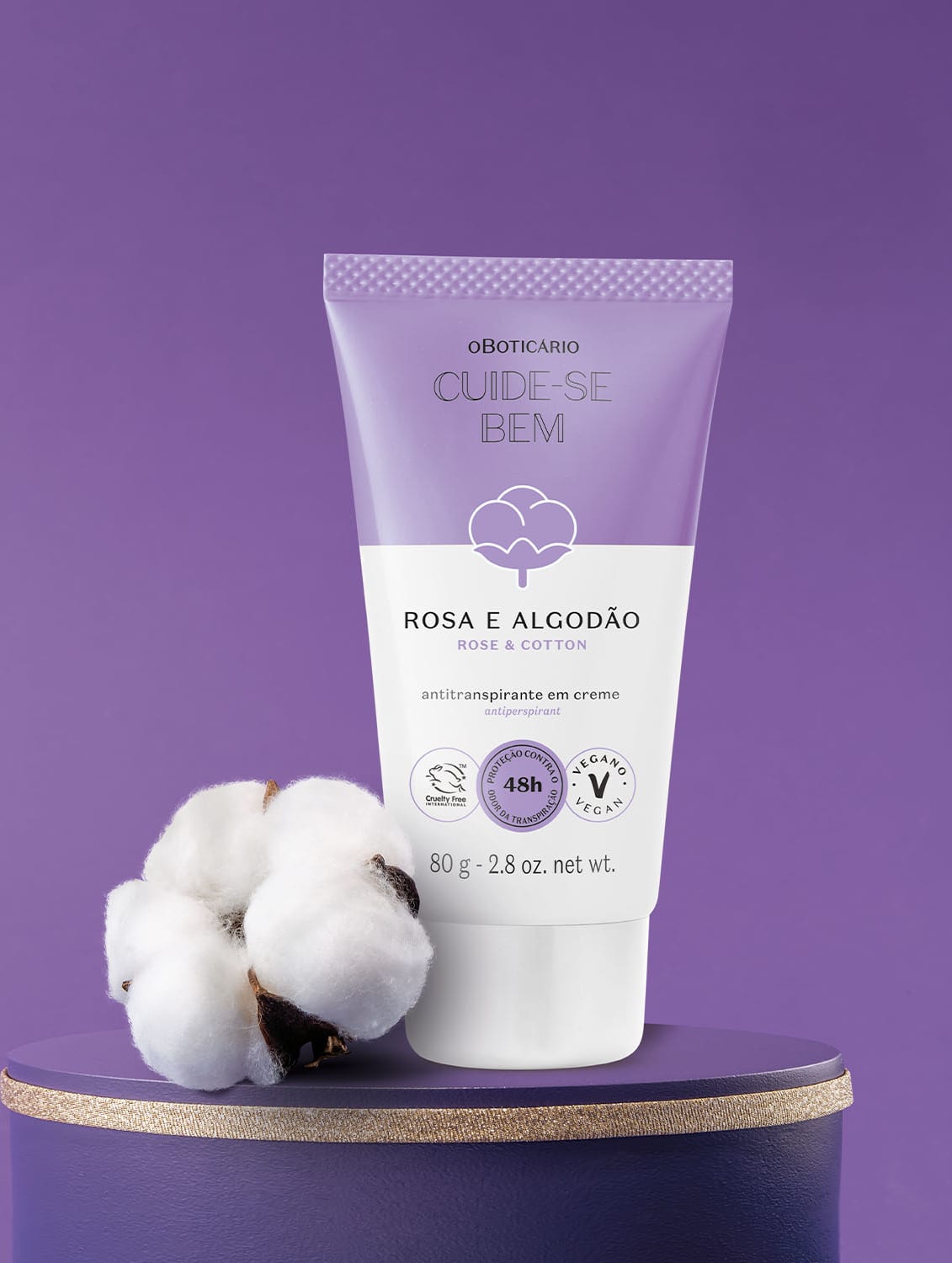 Bisnaga em tons de lilás e branco com flor de algodão ilustrada contendo 80g de antitranspirante em creme da marca Cuide-se Bem Rosa e Algodão. Ao lado da embalagem há flores de algodão e tudo está em superfície e fundo azul escuro.