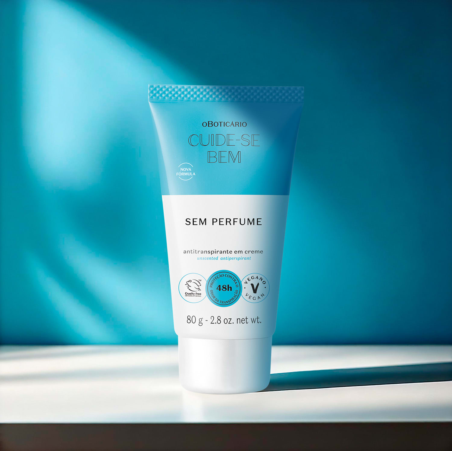 Bisnaga branca e azul com letras pretas de desodorante em creme sem perfume Cuide-se Bem em superfície branca e fundo escura em tons de azul com pouca luz natural.