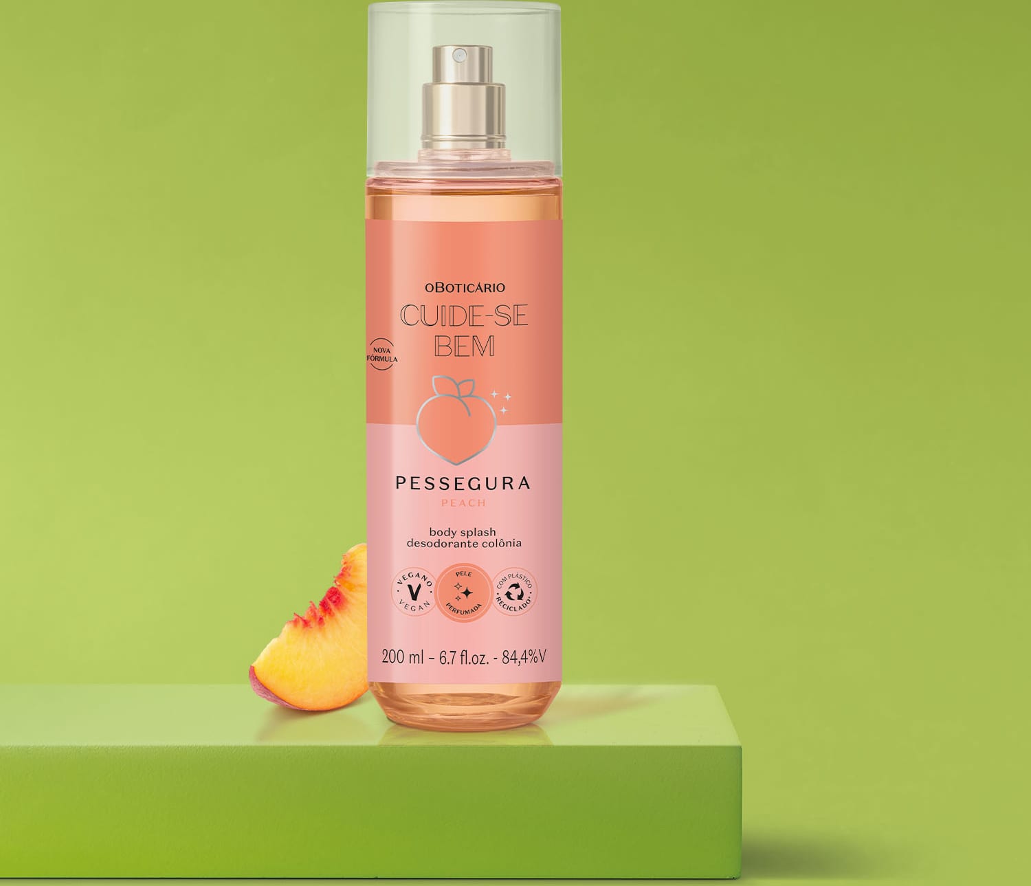 Frasco cilíndrico transparente com líquido rosa, pulverizador prateado, tampa transparente e rótulo em tons de rosa com pêssego ilustrando de body splash Cuide-se Bem Pessegura em fundo verde com pêssego cortado ao lado.