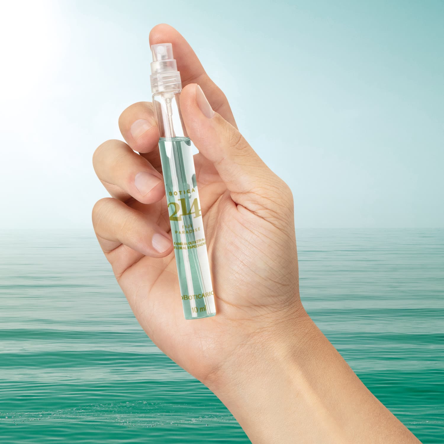 Vidro cilíndrico transparente com líquido azul, tampa preta e letras douradas contendo 10ml de Eau de Parfum masculino Fougére Especiado da marca Botica 214 Fiji Paradise. O fundo da imagem simula água e céu azul.
