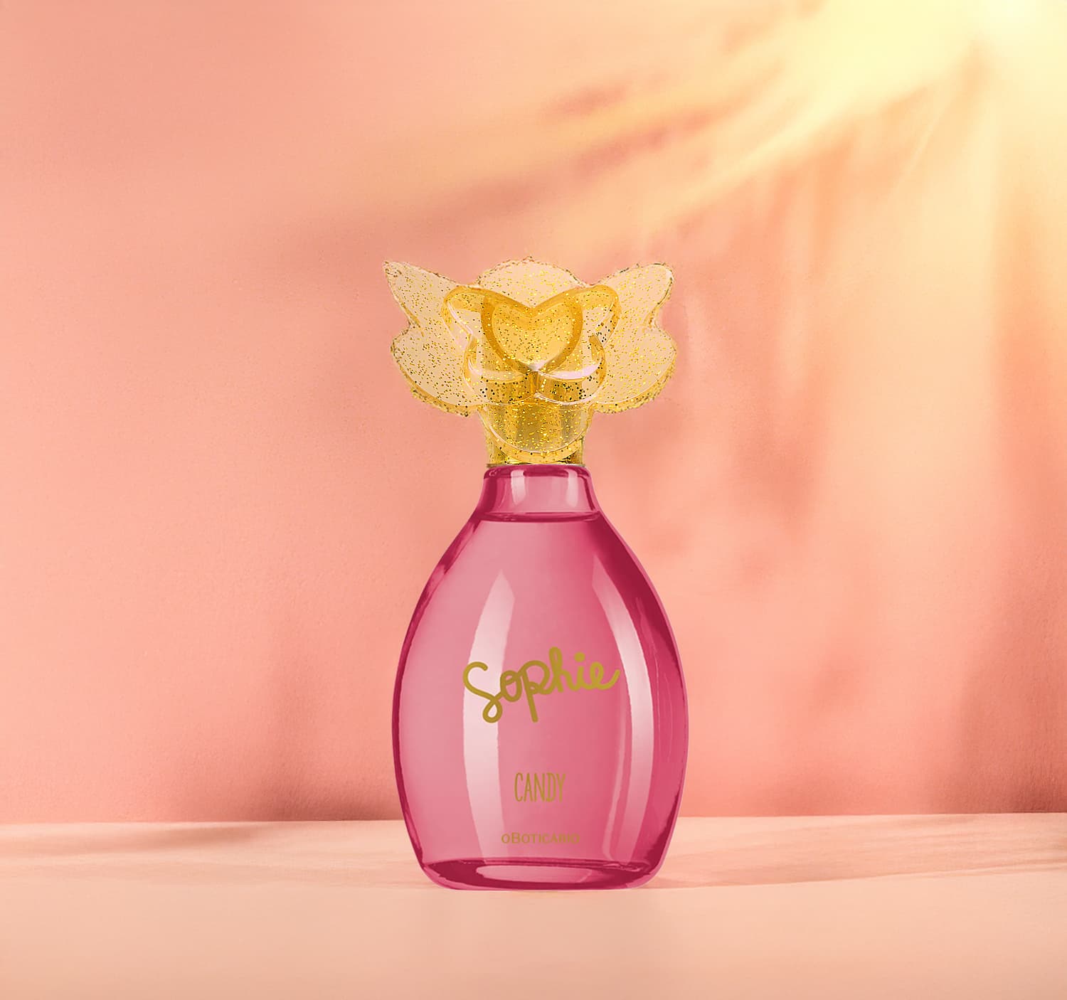 Frasco de colônia infantil Sophie Candy rosa com tampa dourada em formato de borboleta, sobre superfície clara em ambiente com iluminação suave e tons de laranja.s