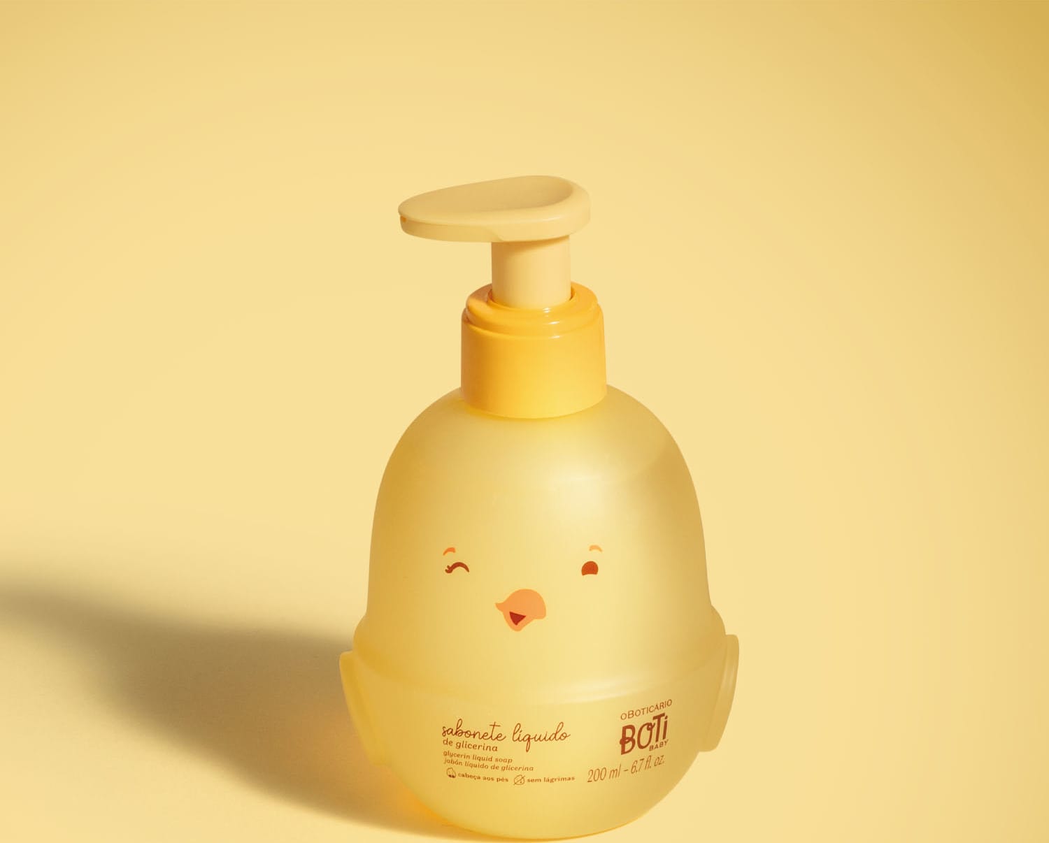 Frasco em forma de passarinho amarelo com detalhes laranjas contendo 200ml de sabonete líquido de glicerina da marca Boti Baby em fundo alaranjado.
