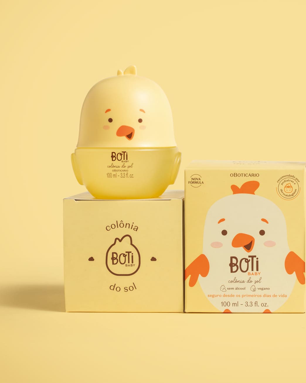 Frasco em formato de passarinho amarelo com parte superior na cor bege escuro e detalhes laranjas de colônia do sol da marca Boti Baby em cima de uma caixa com o nome da marca e ao lado da caixa do produto com ilustração de passarinho.