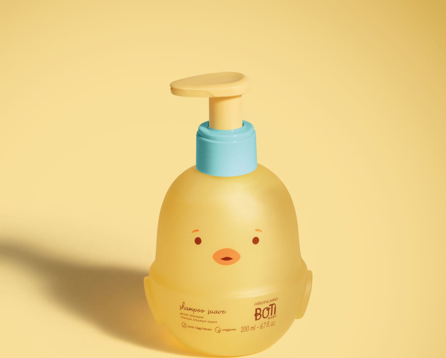 Frasco em forma de passarinho amarelo com detalhes laranjas, tampa azul e bomba dosadora amarela de shampoo suave da marca Boti Baby em fundo alaranjado.