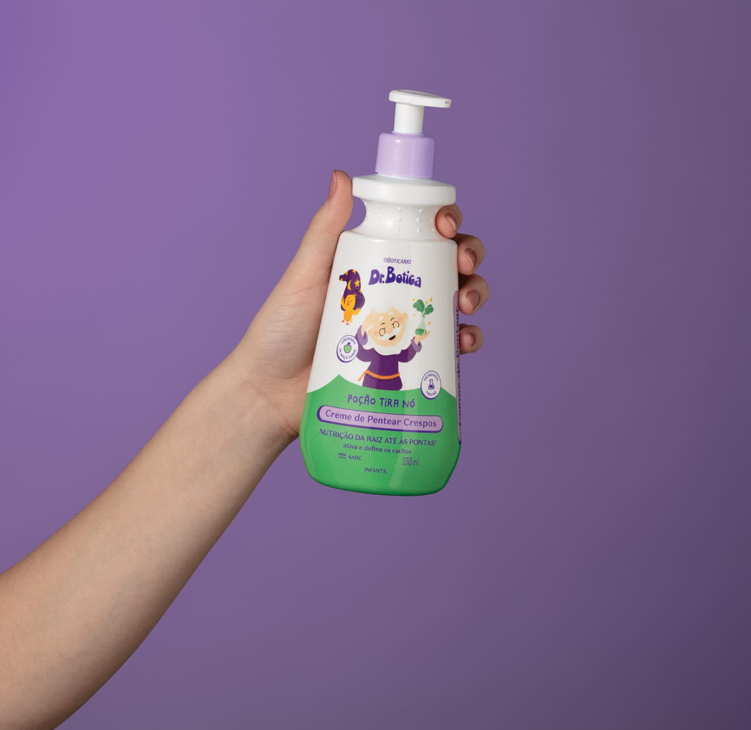 Imagem de uma mão segurando uma embalagem branca e verde com válvula dosadora roxa de creme de pentear infantil para cabelos crespos da marca Dr. Botica em fundo azul escuro.