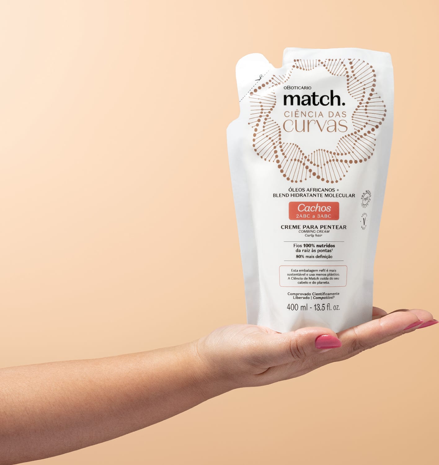 Mão segurando um Refil de creme para pentear para cabelos cacheados Match Ciência das Curvas em sachê branco com letras marrons e detalhes laranjas em fundo rosado.