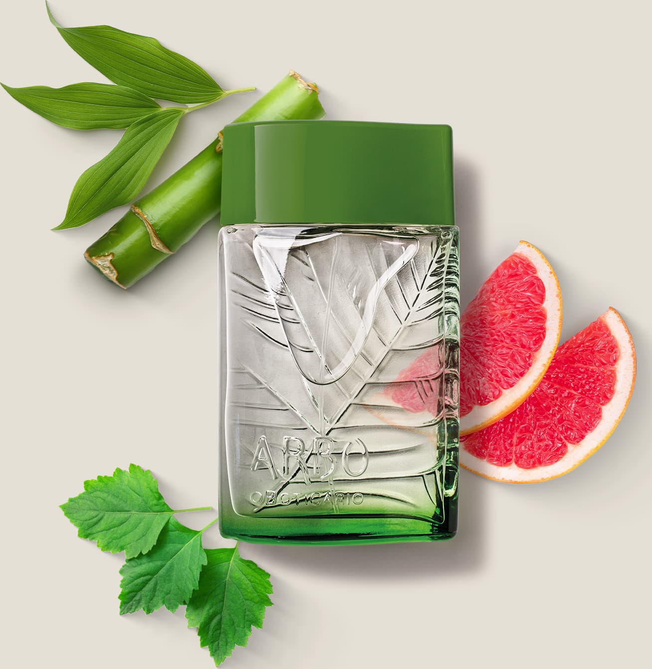 frasco verde transparente com líquido claro, folhagens em relevo e tampa verde escuro contendo desodorante colônia Arbo Puro com folhas verdes e fatias de toranja rosa ao redor, sobre superfície clara.