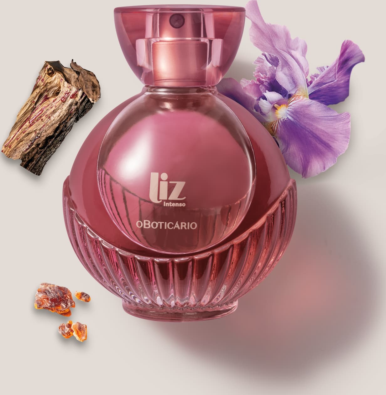 Um vidro com líquido vermelho, borrifador dourado, tampa transparente e letras douradas de desodorante colônia Liz Intenso está em um fundo cinza com flor roxa, pedaço de madeira e âmbar ao redor.