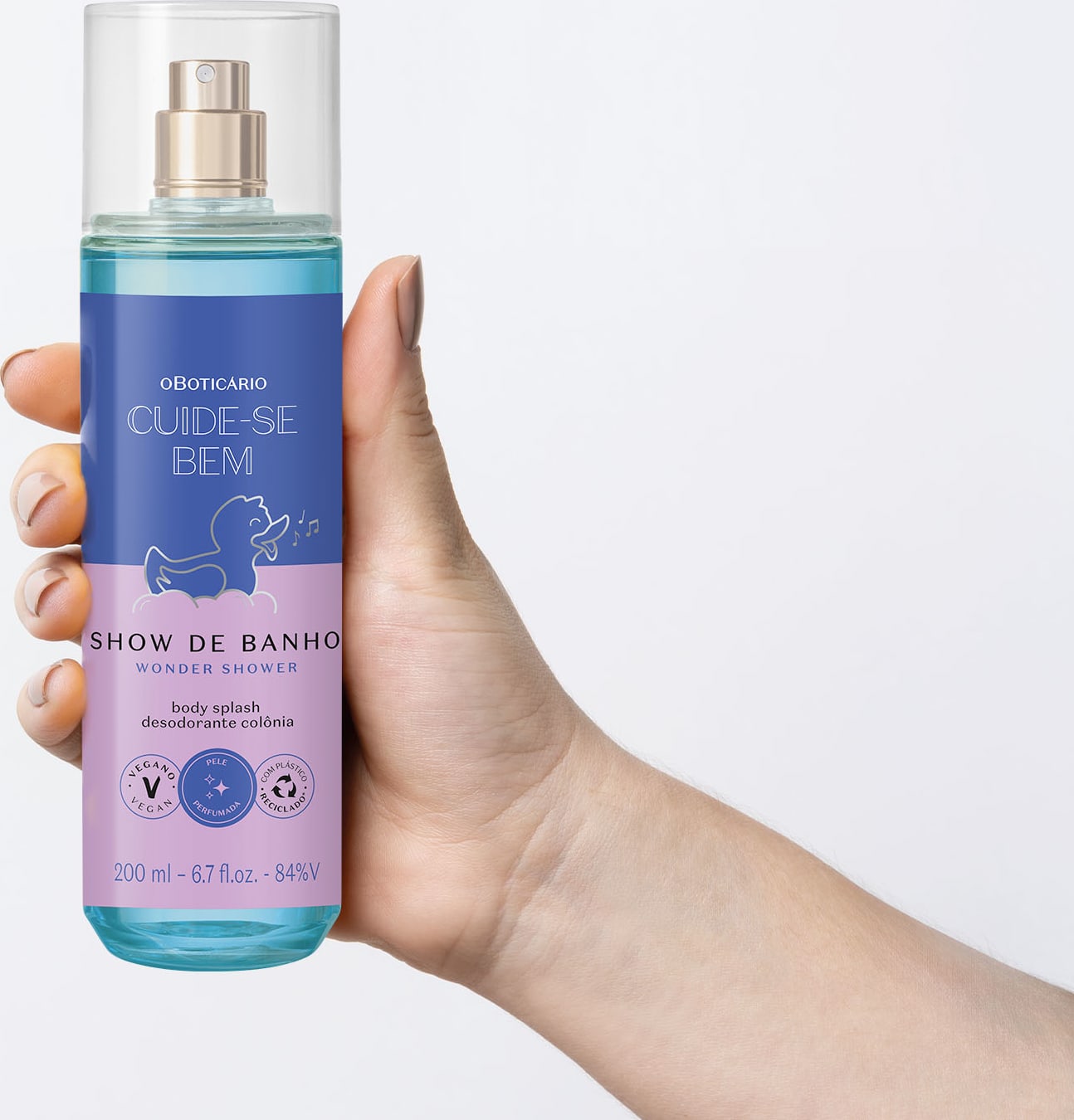 Mão segurando um Frasco com líquido azul, pulverizador prateado, tampa transparente e rótulo azul e lilás com patinho de banho ilustrado de body splash da marca  Cuide-se Bem Show de Banho em fundo azul claro.