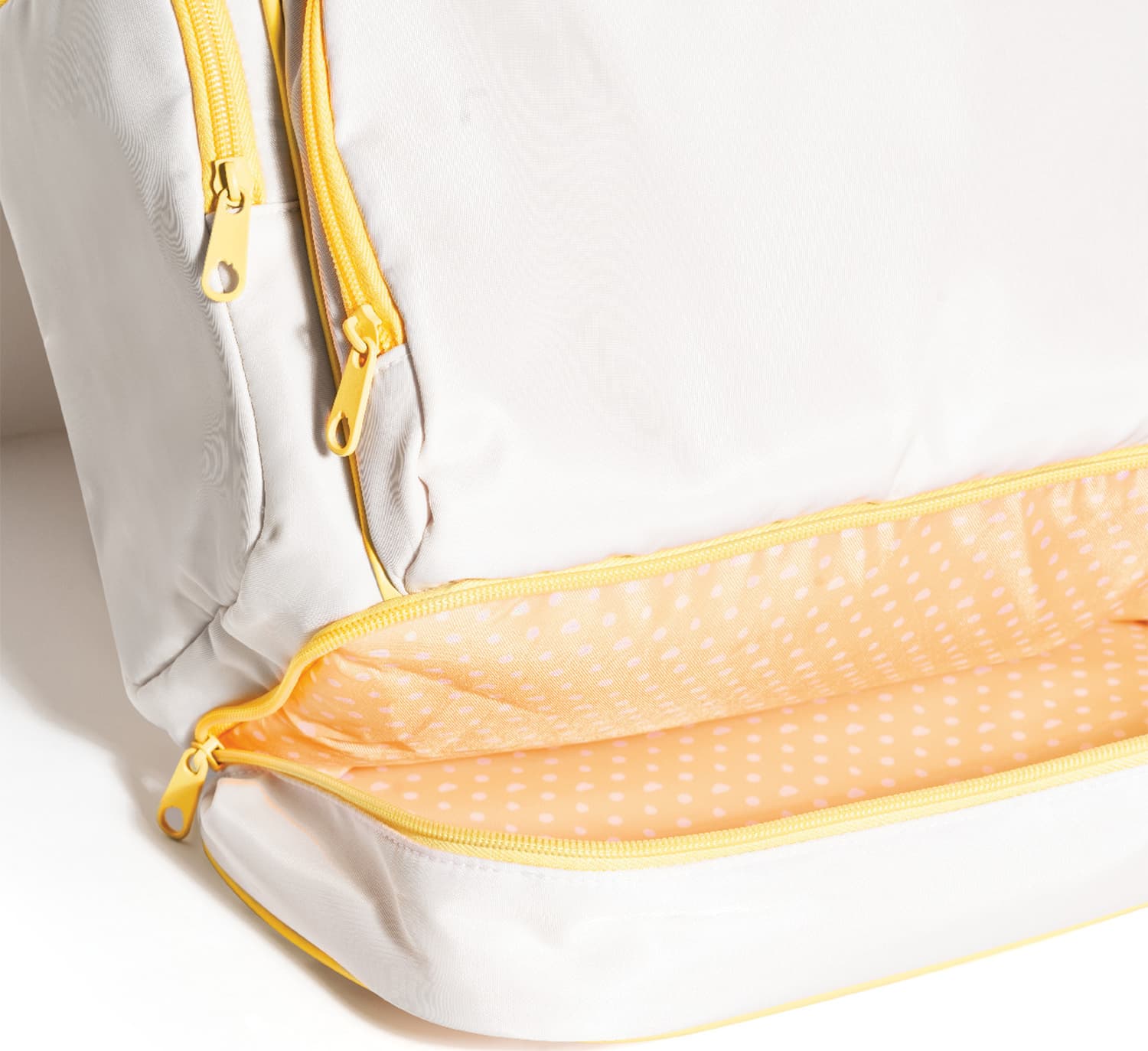 Close-up de Mochila branca com detalhes em amarelo com bolso frontal do fundo da mochila aberto revelando um revestimento amarelo de bolinhas brancas.