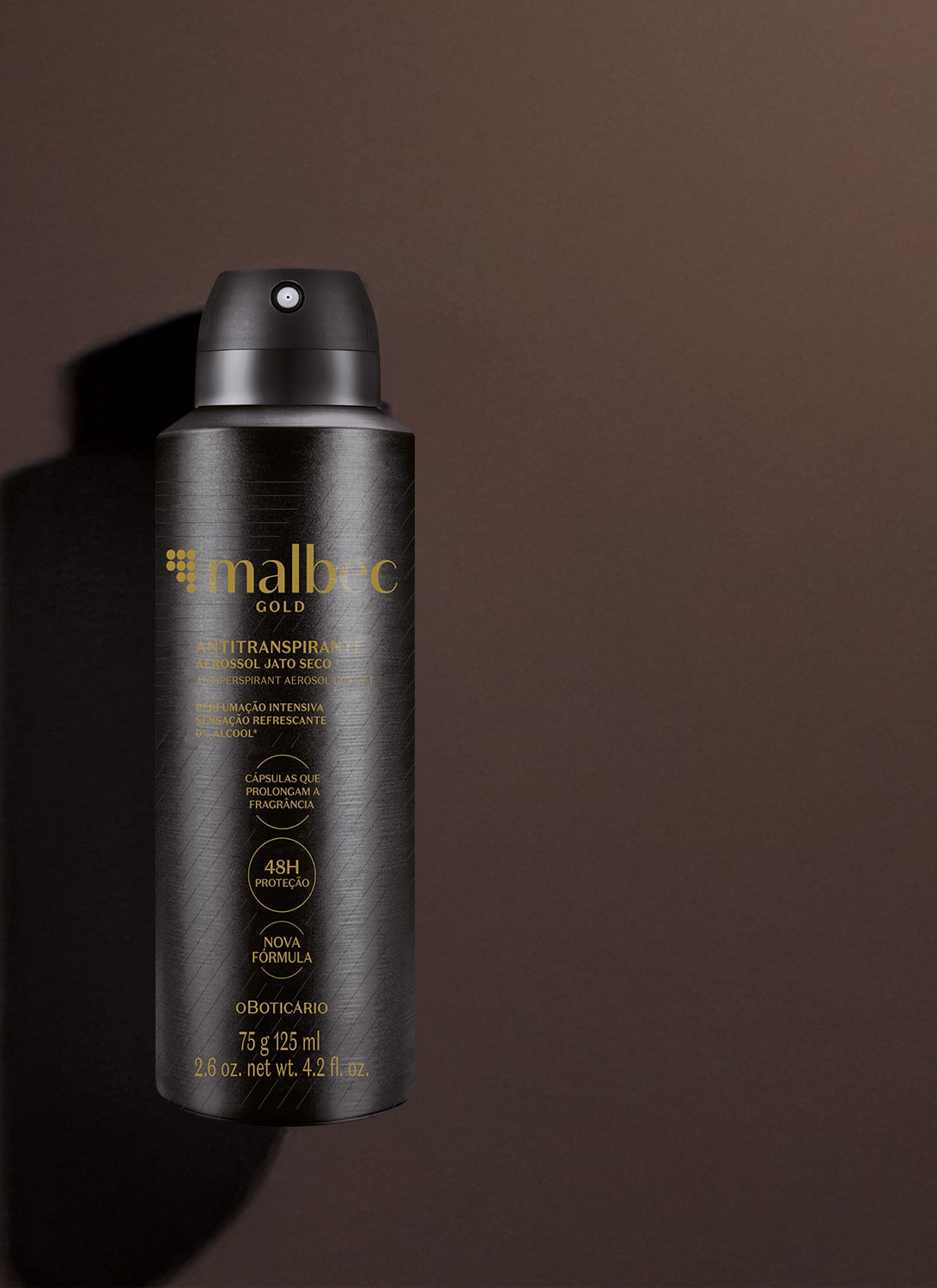 Imagem de um frasco preto de desodorante antitranspirante aerossol da marca Malbec Gold, com rótulo em dourado. Ele está em um fundo cinza escuro e há uma sombra, compondo um cenário forte e elegante.