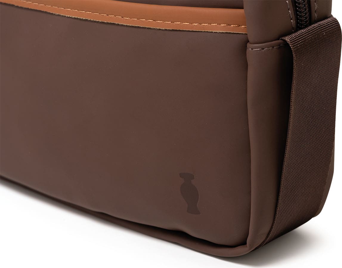 Bolsa tipo nécessaire retangular na cor marrom escuro e detalhes marrom claro com alça de transporte e zíper.