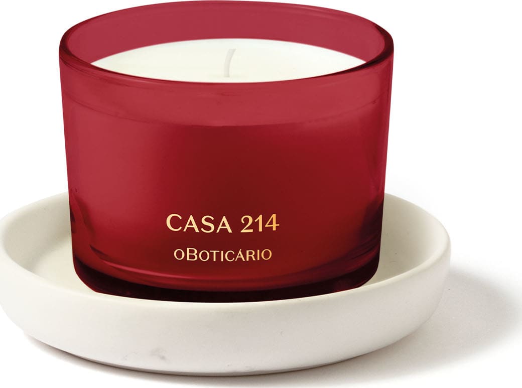 Vela perfumada branca em recipiente vermelho acompanhada de um suporte para velas branco, ambos da marca Casa 214.