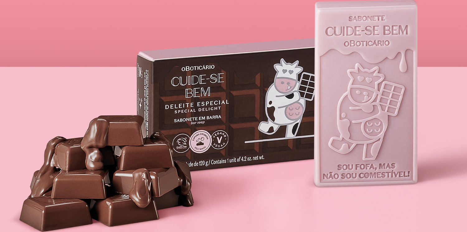 Sabonete em barra de chocolate com embalagem especial. Embalagem marrom com ilustração de uma vaca usando um avental e segurando uma barra de chocolate. Sabonete com ilustração de uma vaca e texto "Sou fofa, mas não sou comestível!".