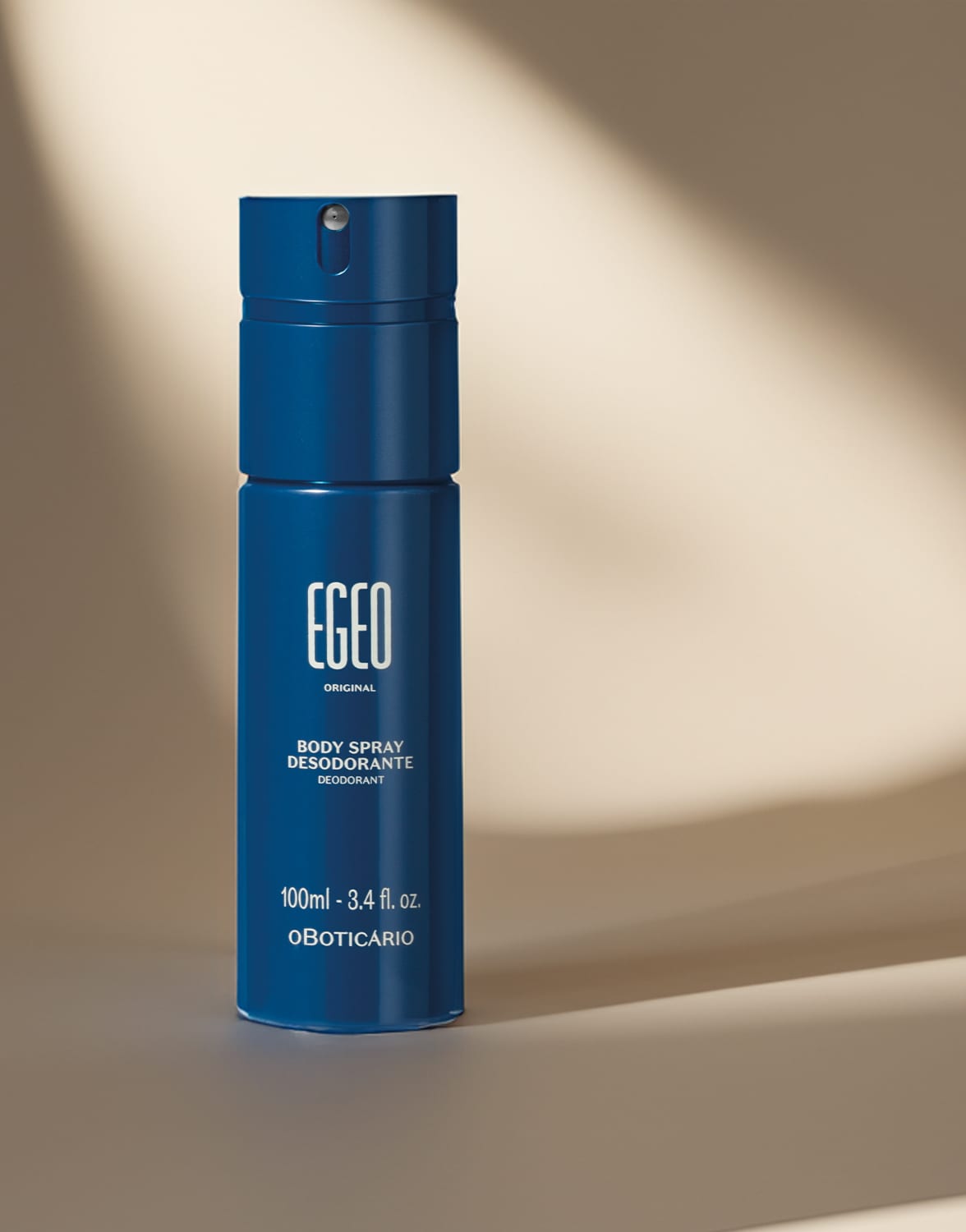 Frasco cilíndrico azul marinho com letras brancas de body spray da marca Egeo Original em fundo escuro com leve luz natural sobre o produto.