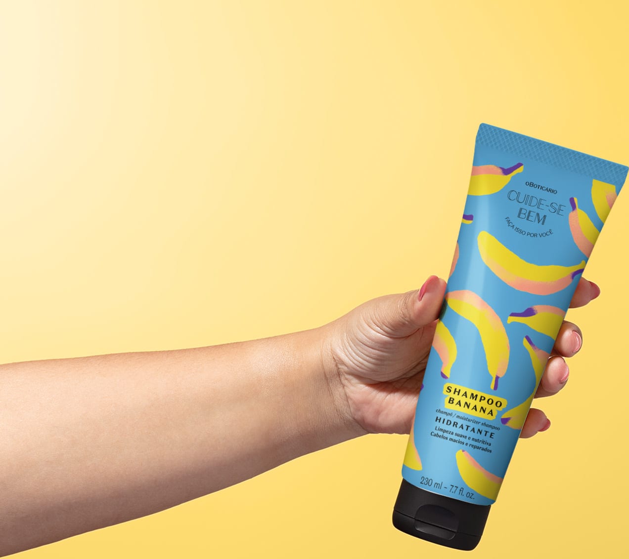Imagem de uma mão segurando um frasco de shampoo hidratante da marca Cuide-se Bem Feira Banana, em embalagem azul com bananas ilustrando, contendo 230 ml do produto. O fundo é em tons de branco e amarelo.