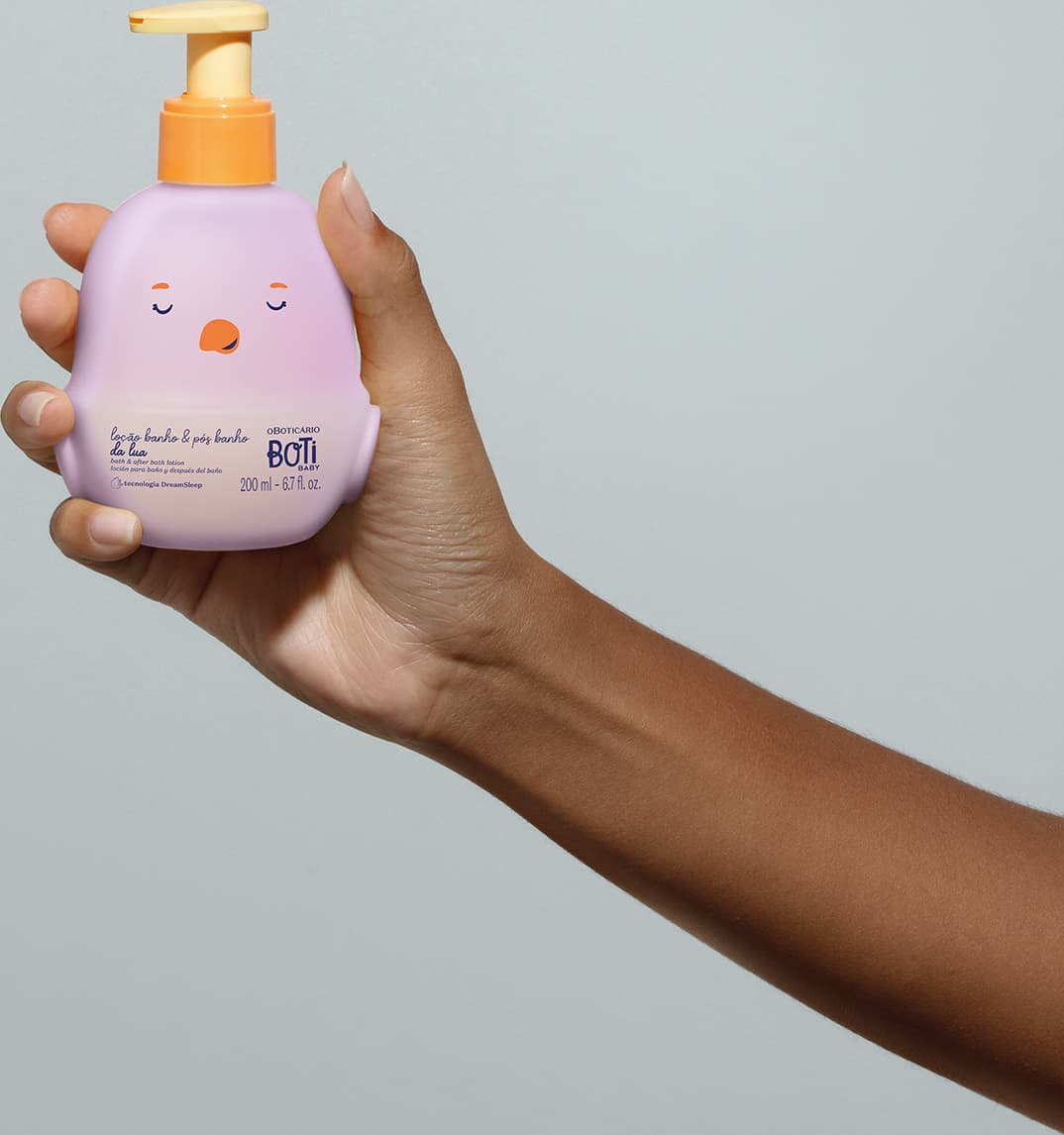 Mão feminina segurando um frasco da loção para banho e pós banho Boti Baby Lua em forma de pintinho na cor lilás e bomba dosadora laranja em fundo lilás.