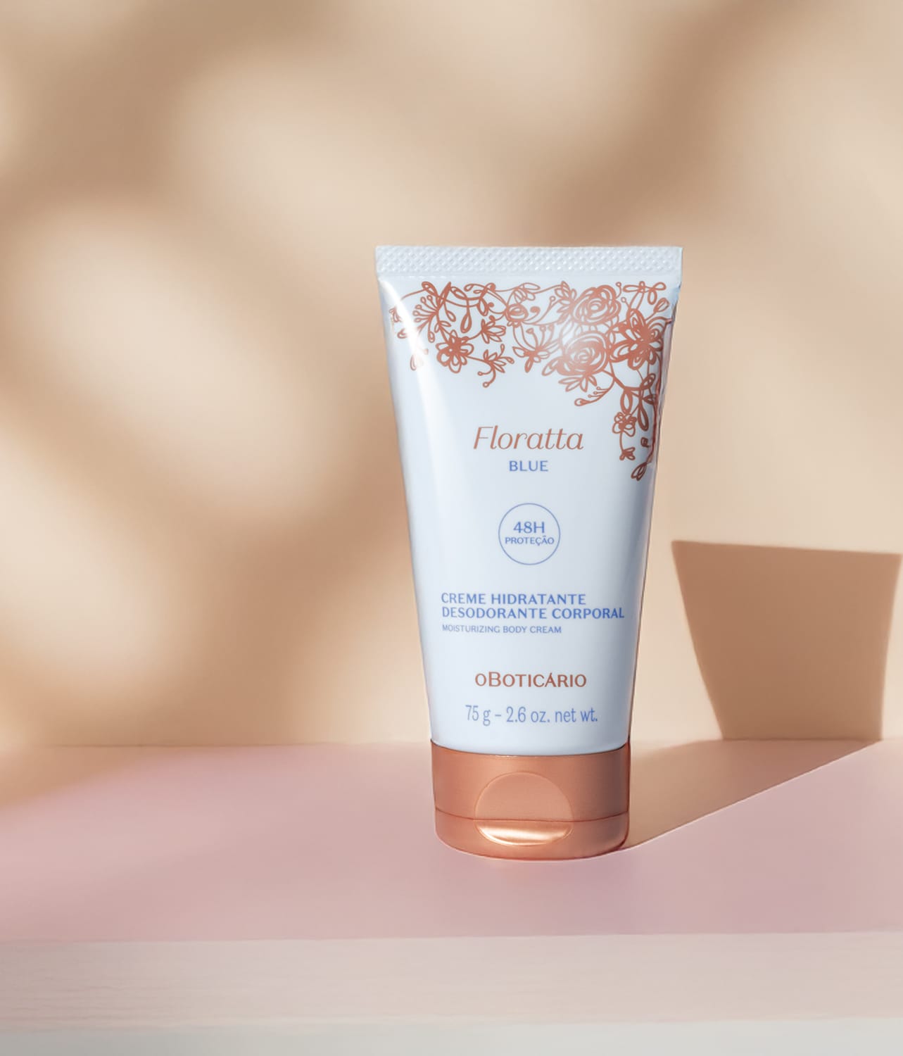 Bisnaga azul claro, letras azuis, detalhe floral e tampa na cor dourada contendo creme hidratante corporal Floratta Blue em fundo bege com sombras.