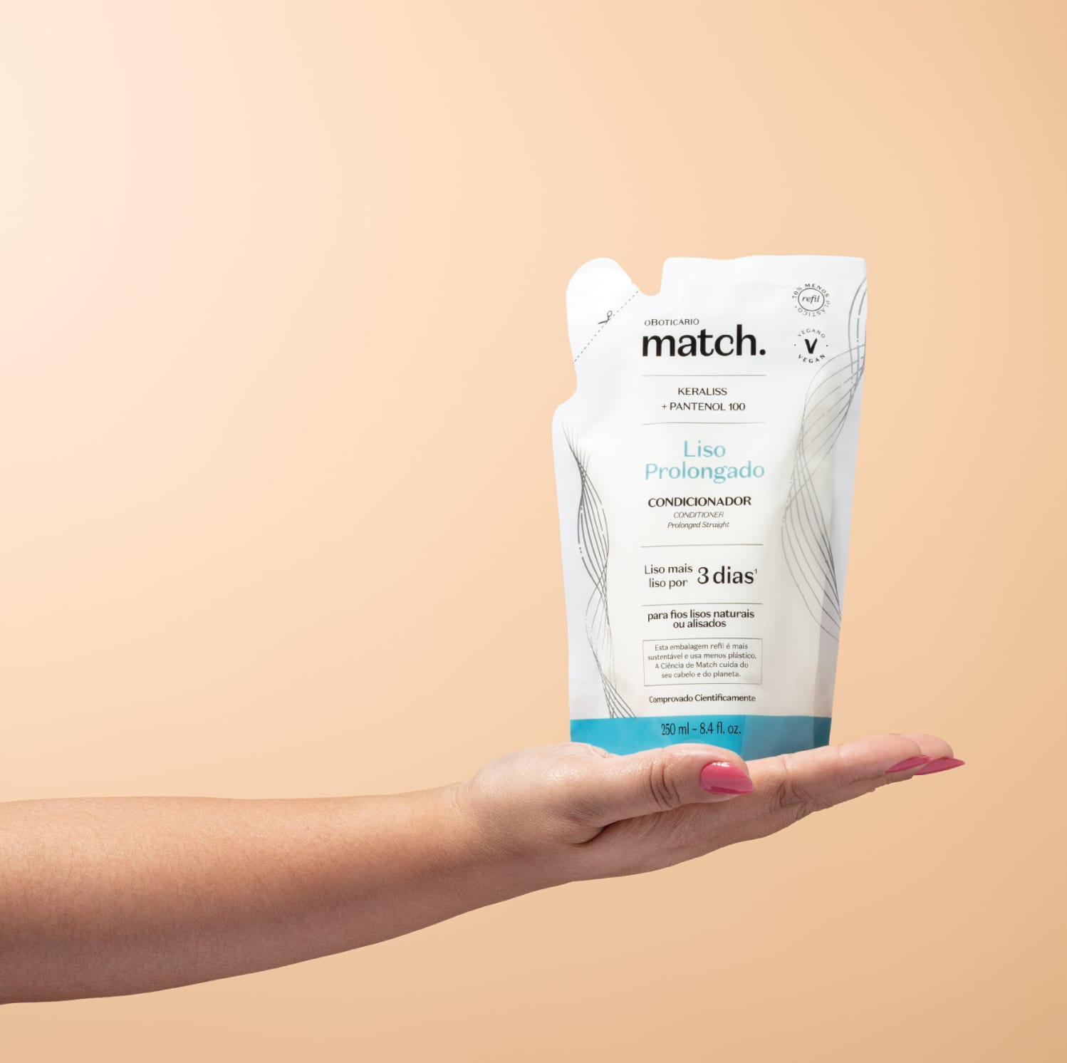 Mão segurando um refil de condicionador Match Liso Prolongado em sachê nas cores azul e branca com letras pretas em fundo em tons de rosa.