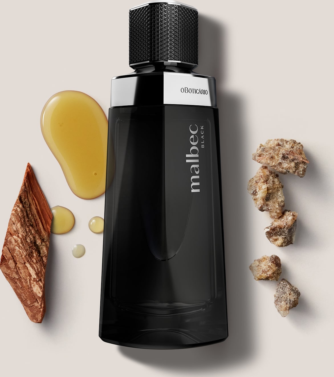 O frasco é preto e possui um design moderno e elegante. Ao redor do frasco, há alguns elementos decorativos, como pedras, madeiras e uma substância líquida amarelada, que parecem ser ingredientes naturais utilizados na composição da fragrância.
