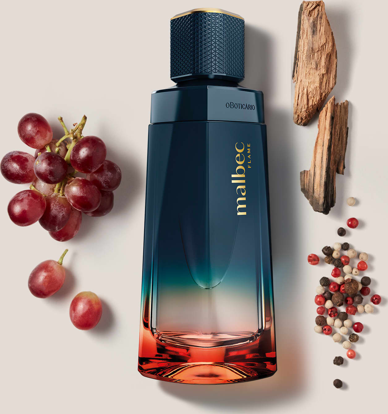 O frasco possui um design elegante e moderno, com uma coloração degradê que vai do azul escuro ao laranja. Está posicionado entre alguns ingredientes naturais, como uvas vermelhas e especiarias, sugerindo uma composição aromática.