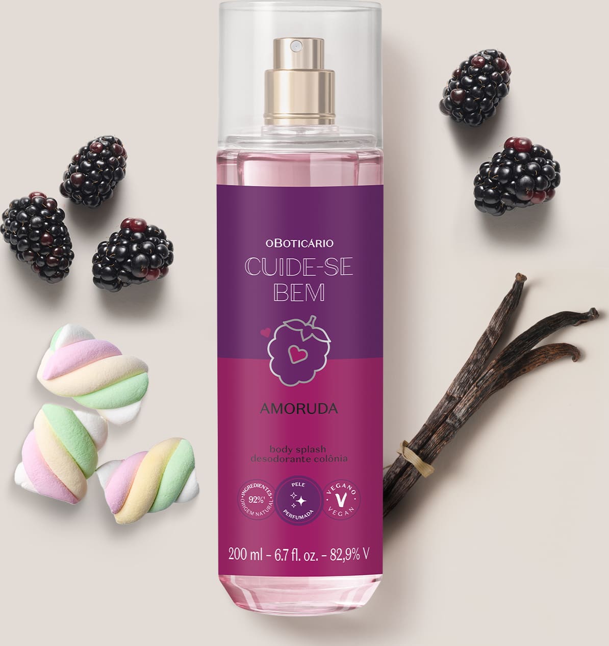 Ambiente de beleza com body splash da marca Cuide-se Bem Amoruda, embalagem roxa com ilustração de amora, rodeado por amoras, marshmallows coloridos e um pedaço de baunilha, sugerindo uma fragrância doce e natural.