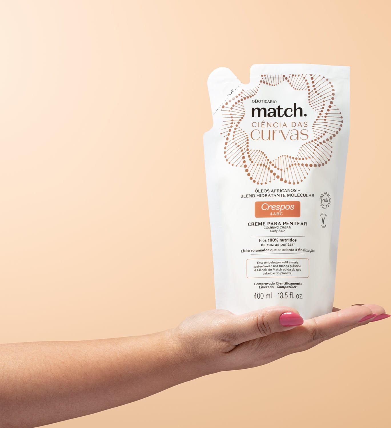 Imagem de uma mão segurando uma embalagem refil branca de creme para pentear da marca Match, com design de círculos e linhas em marrom, informando "Ciência das Curvas" e "Crespos 4ABC" no rótulo. O fundo é rosa bem claro.