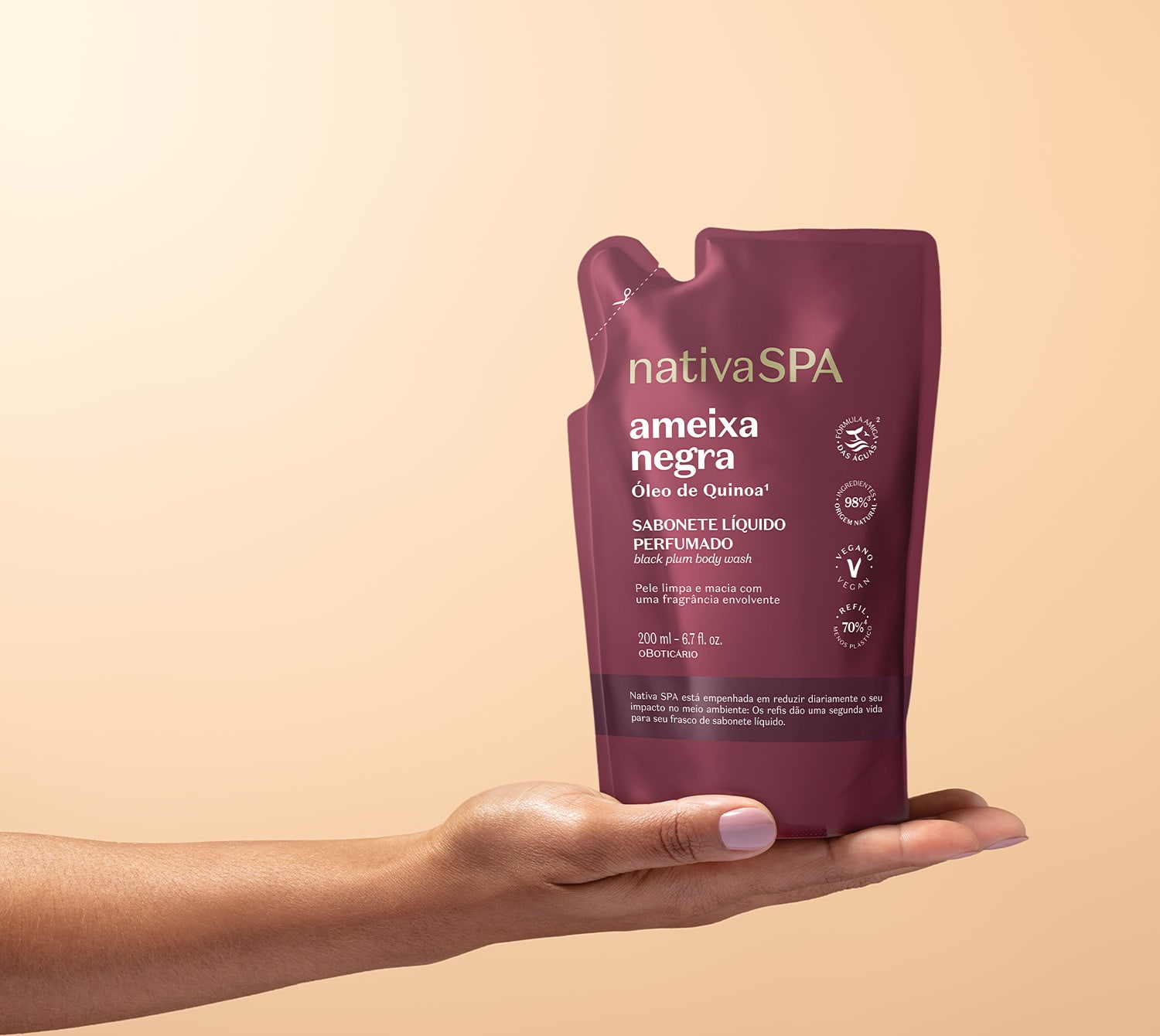 Imagem de uma mão segurando uma embalagem refil de sabonete líquido perfumado da marca Nativa SPA, na cor vinho, com rótulo destacando o nome "Ameixa Negra". O fundo é em tons de branco e rosa.