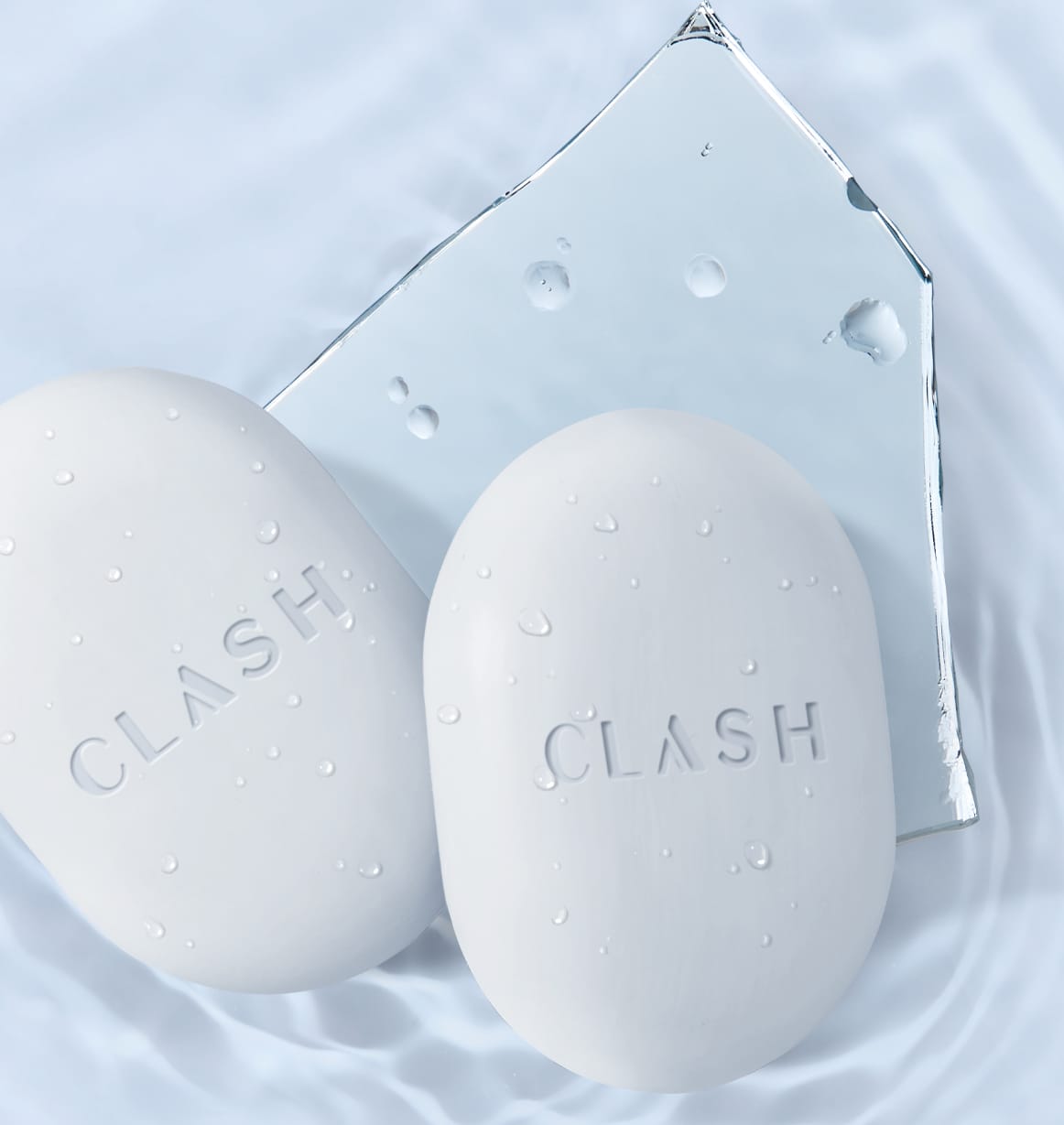 Dois sabonetes brancos com a marca "Clash" em relevo, flutuando sobre uma superfície aquática com gotas d'água, em uma superfície clara e molhada