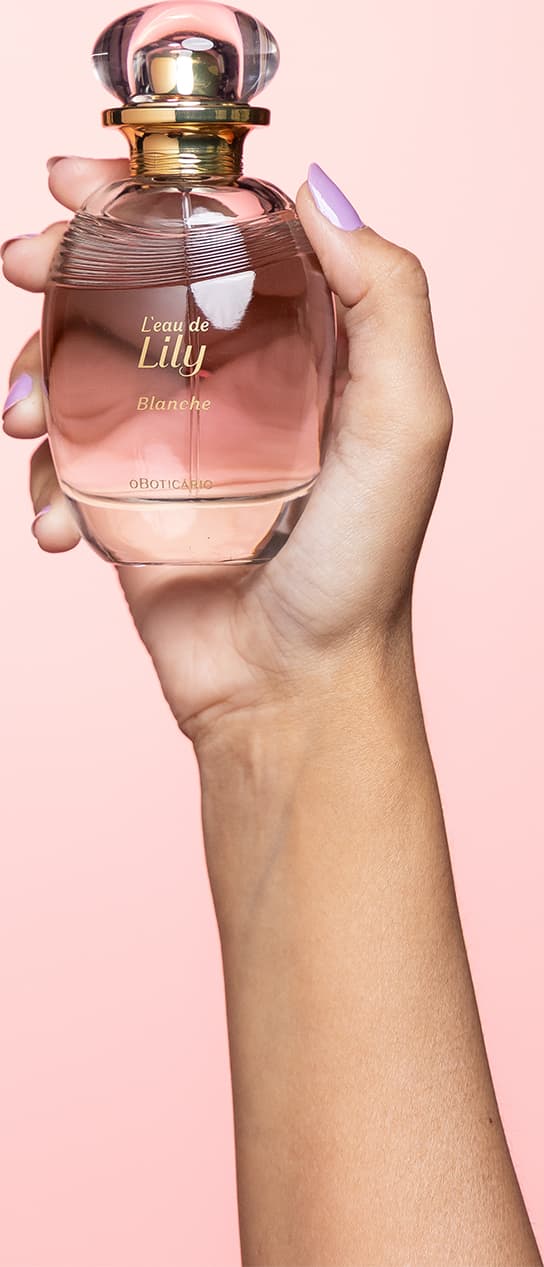 A cor predominante do frasco é um tom rosado, que transmite uma sensação delicada e feminina. A fragrância é segurada por uma mão feminina, com unhas pintadas em uma cor clara, indicando se tratar do desodorante colônia L'eau de Lily Blanche.
