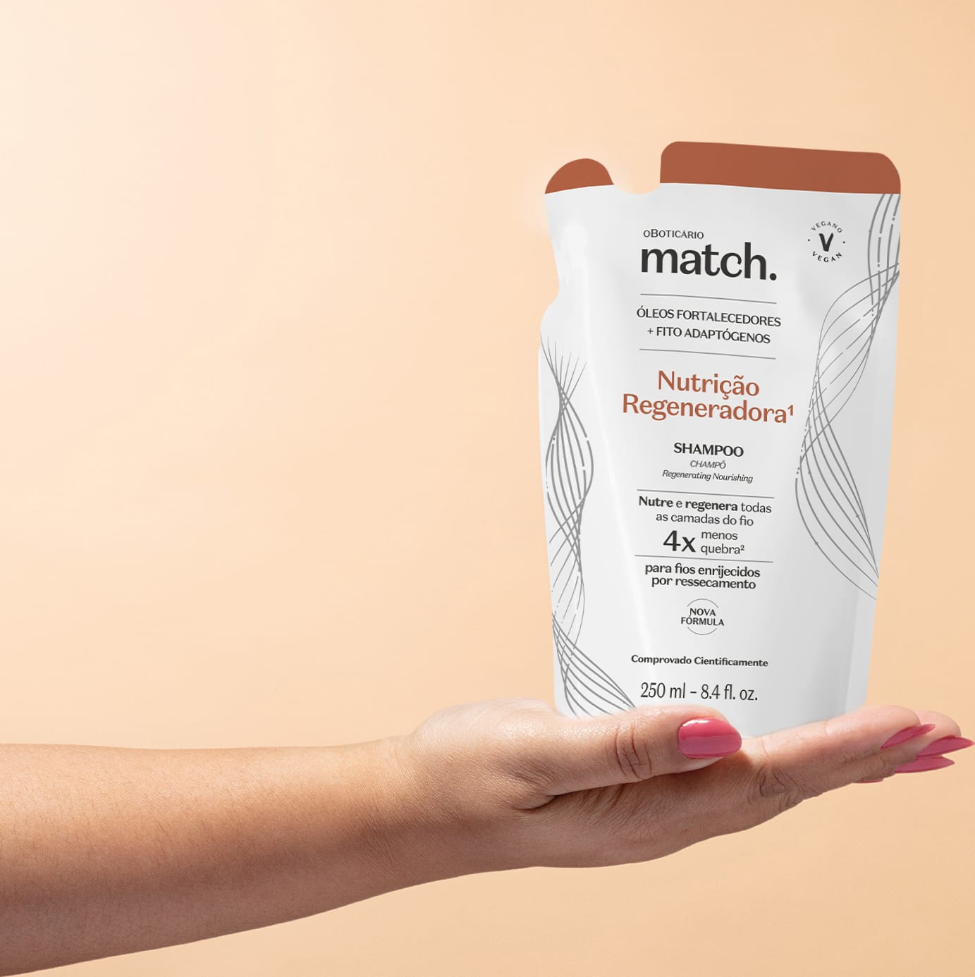 Imagem de uma mão feminina segurando um refil em forma de sachê na cor branca com detalhes laranja e letras pretas contendo shampoo da marca Match. Nutrição Regeneradora. O fundo da imagem é rosa.