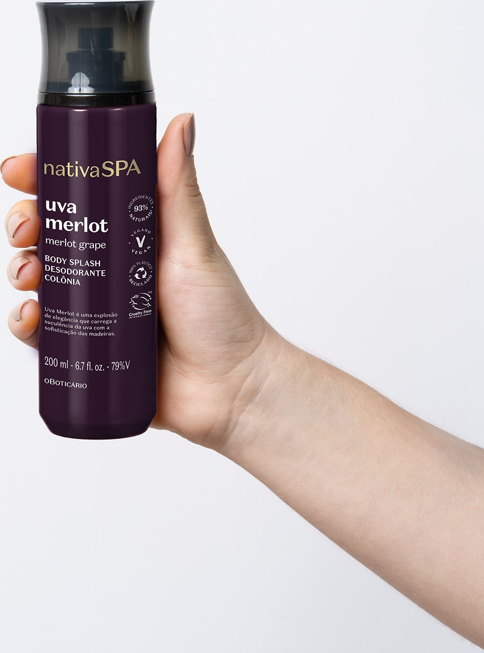Mão segurando um frasco preto e roxo com letras brancas e douradas contendo loção hidratante corporal Nativa SPA Uva Merlot.