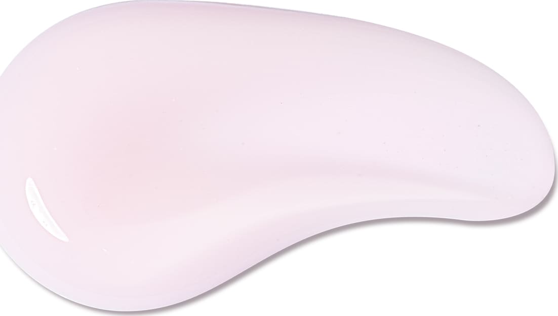 O produto de beleza apresenta uma textura suave e cremosa, com uma cor rosa pálida uniforme. Sua aparência é lisa e sedosa, sugerindo uma consistência delicada e agradável ao toque.