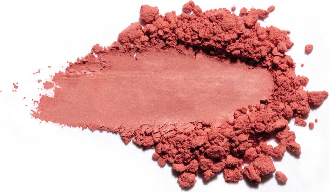 Textura de pó rosa-avermelhado com acabamento acetinado e superfície irregular, espalhada sobre fundo branco.