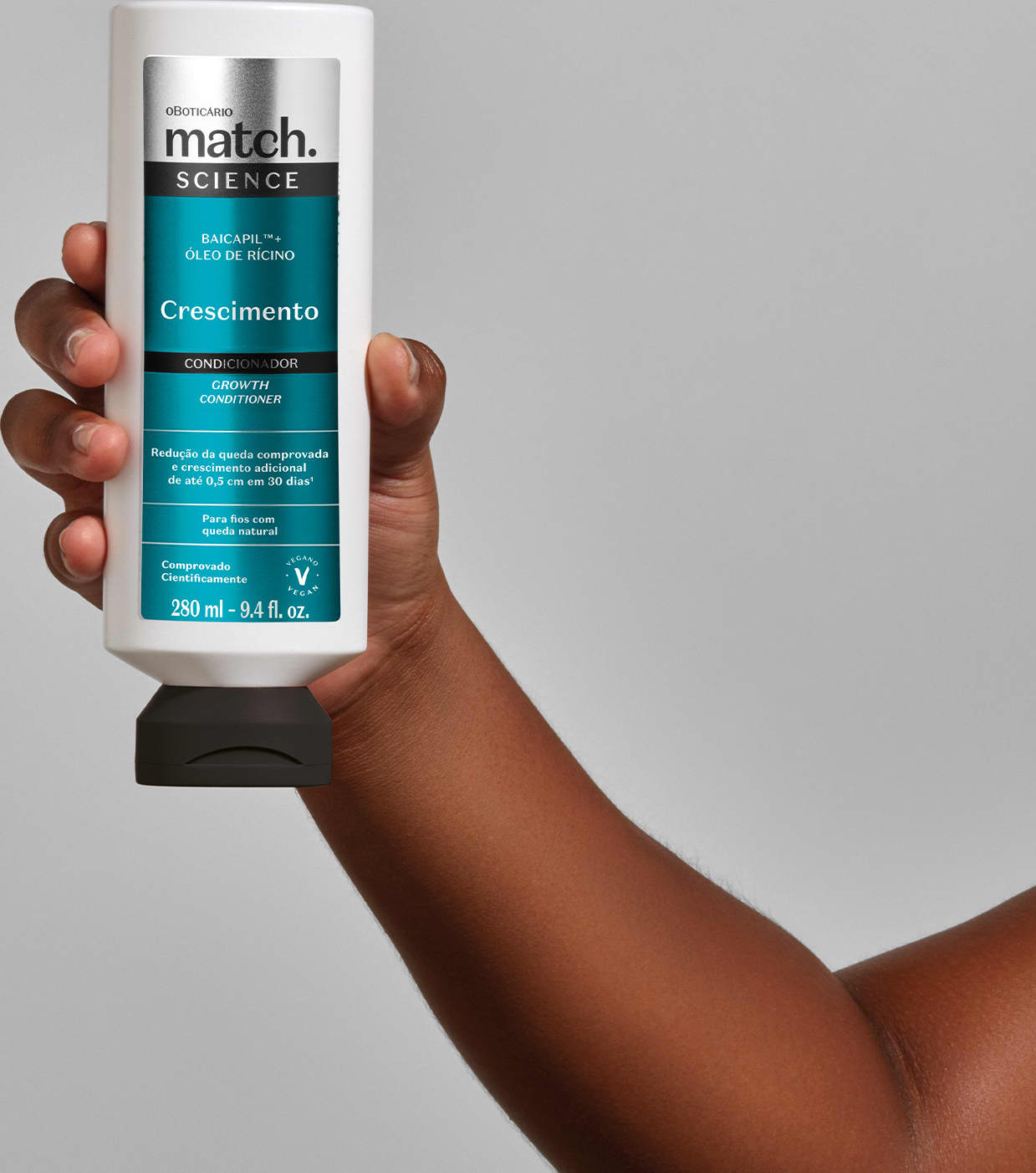 Embalagem de condicionador na cor branca com rotulo azul da linha Match Science Crescimento. O produto está sendo segurado de frente por mão feminina negra em fundo cinza claro.