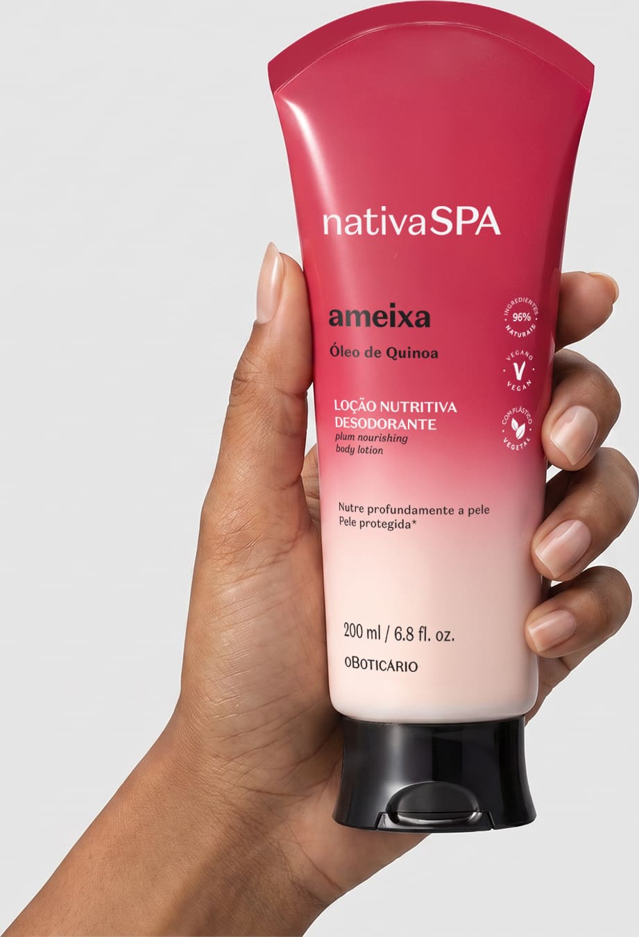 Bisnaga de loção corporal Nativa SPA em degradê de vermelho para o branco sendo segurada por mão feminina negra, mostrando a frente da embalagem sobre fundo branco.