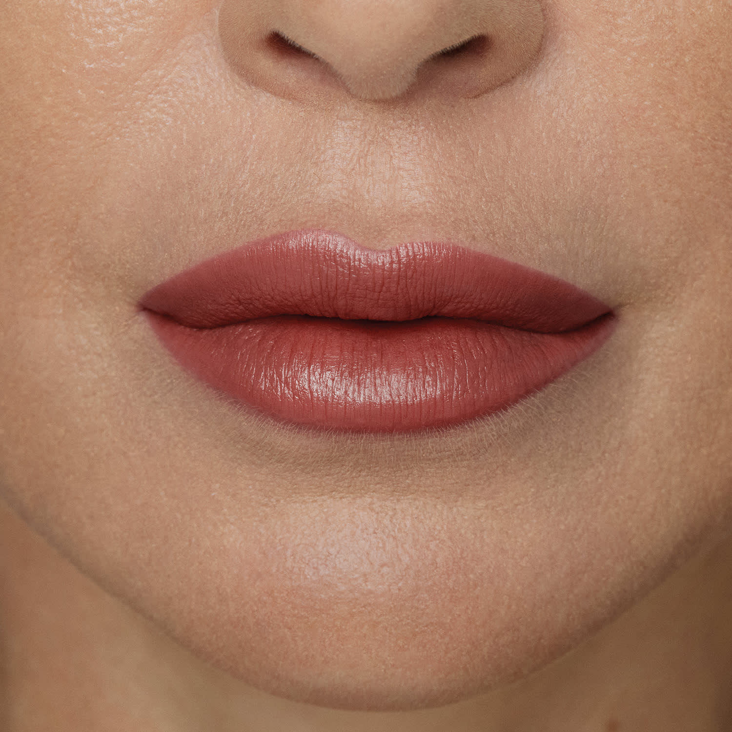 Boca feminina de mulher branca em close mostrando queixo e um pedaço do nariz, com boca fechada, expressão séria e lábios com batom rosado sobre eles.