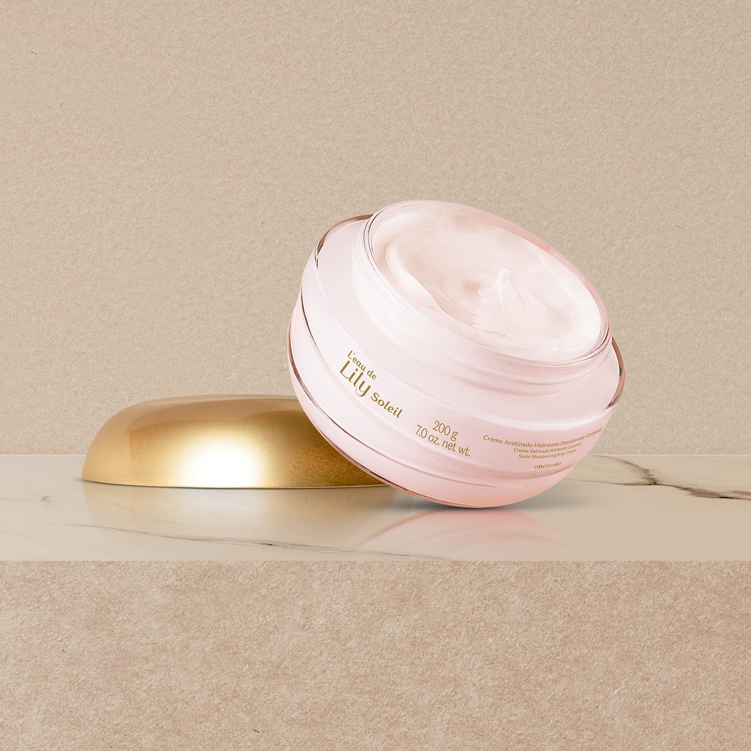Imagem do pote transparente de creme acetinado corporal L'eau de Lily Soleil aberto sobre superfície de mármore bege, com a tampa dourada ao lado.
