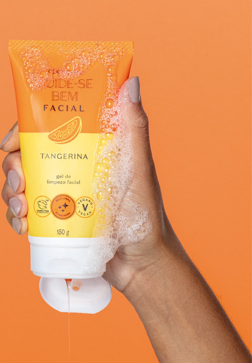 Imagem do tubo de gel de limpeza facial da marca Cuide-se Bem Tangerina em fundo laranja, sendo segurado por mão feminina com unhas pintadas de tom claro. A embalagem é laranja e amarela e possui tampa branca.