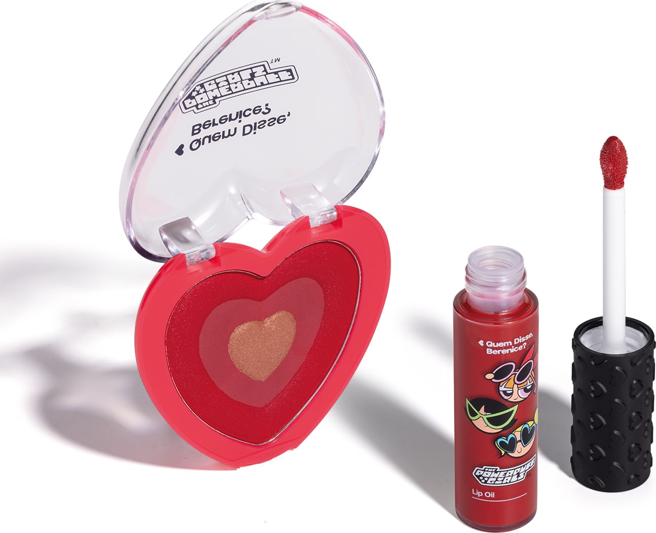 Imagem de dois itens da marca QDB As Meninas Super Poderosas, sendo um blush compacto rosa em formato de coração e um lip oil vermelho com aplicador em forma de esponja na cor vermelha. O fundo da imagem é branco com sombreado.