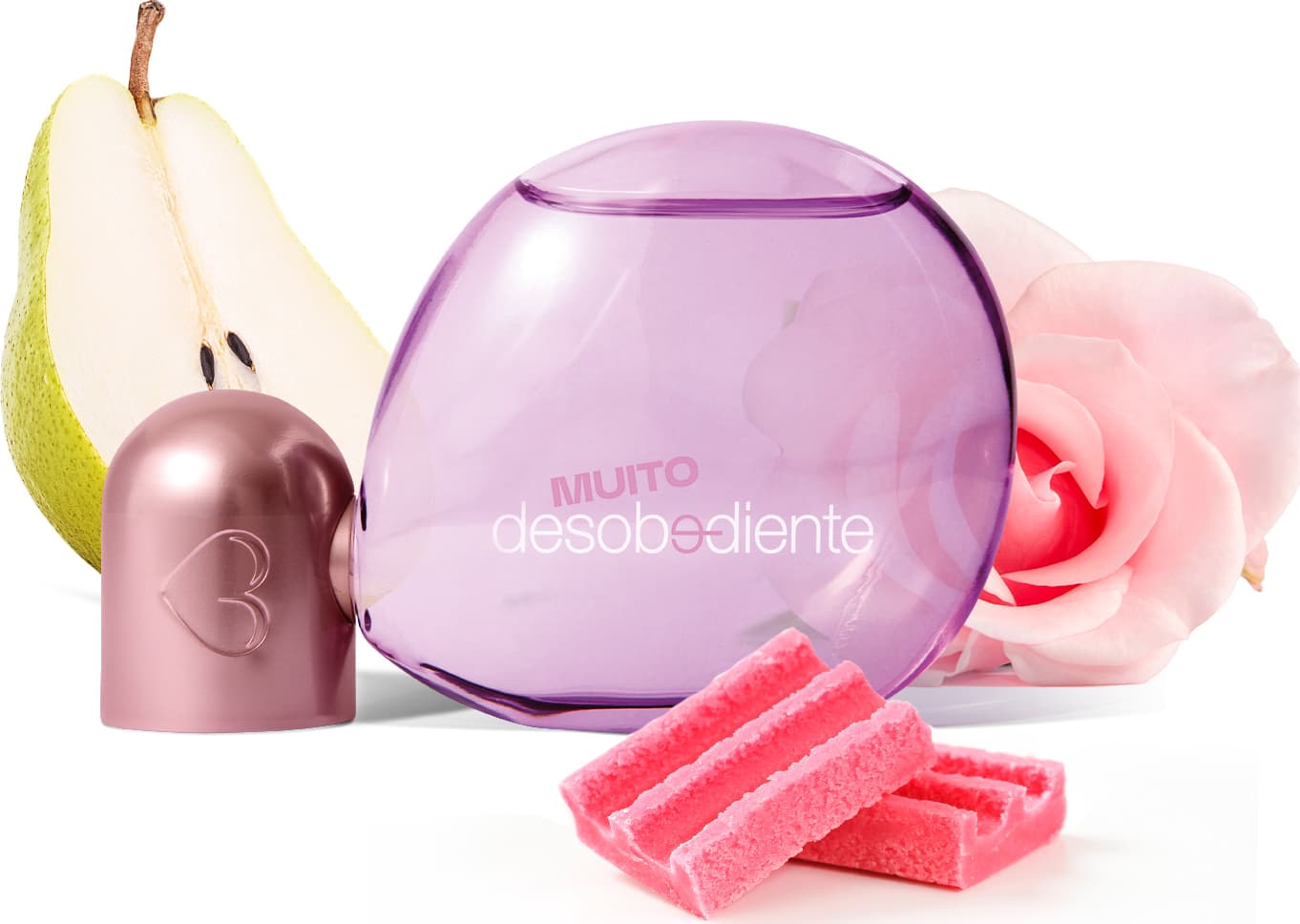 Recipiente rosa com detalhes metalizados de Eau de Parfum Muito Desobediente, acompanhado de uma pera verde, flores rosas e balas vermelhas sobre uma superfície branca.