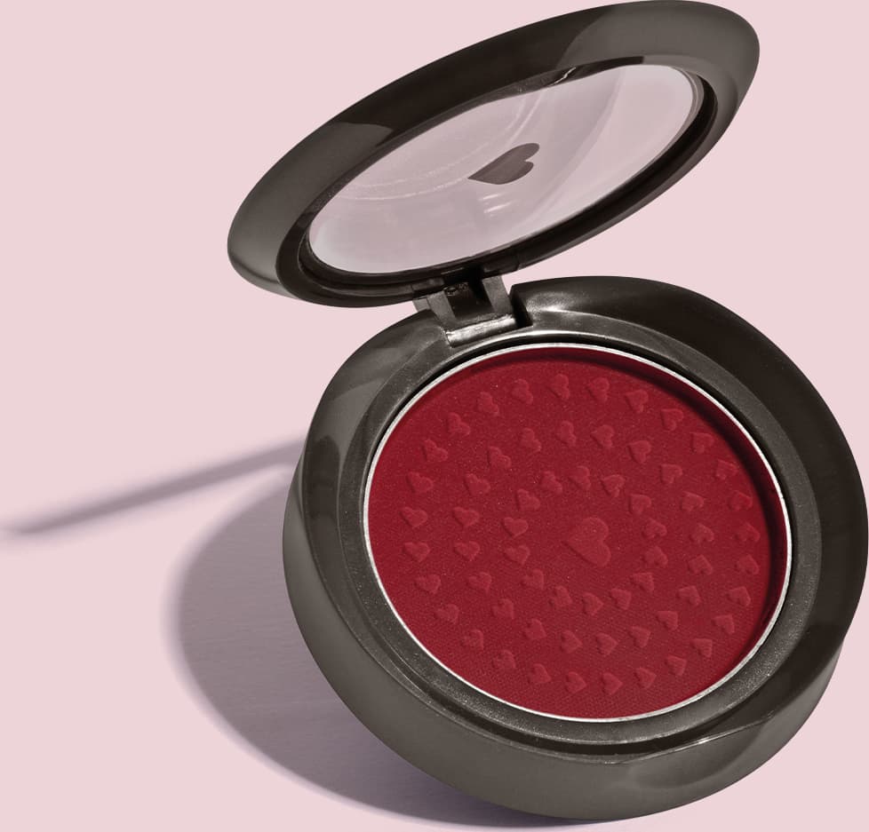 Estojo compacto redondo na cor preta com tampa transparente com coração ilustrado contendo 2g de blush em pó compacto Rubor Vermelho Vermetin da marca Quem Disse, Berenice? em fundo lilás.